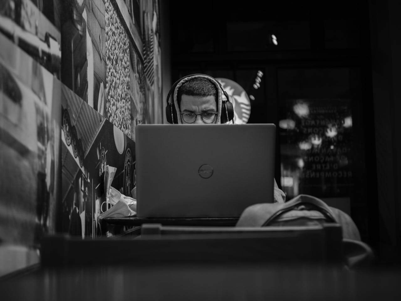 Black and white photo of a man working remotely in a Montreal cafe using his laptop and headphones.